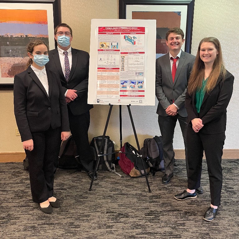 Four students standing beside their poster project