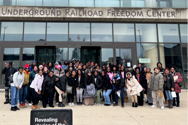 Group photo of students standing in front of a museum with glass windows and an overhead sign that says “Underground Railroad Freedom Center